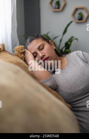 A migrant worker, exhausted from a full day's work, rests peacefully on the sofa. Her tired expression reflects the hard labor she endures for a bette Stock Photo