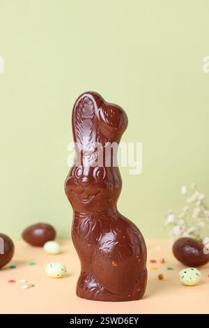 Chocolate Easter bunny with eggs and flowers on table against green background Stock Photo