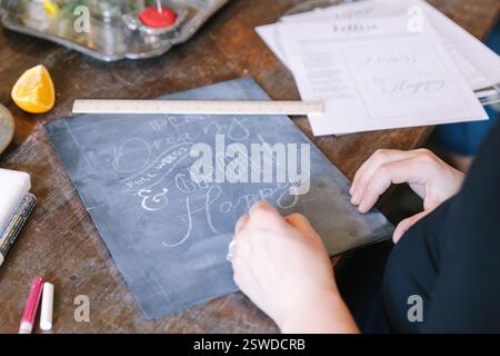 Participants are engaged in a creative workshop practicing hand lettering on slate, showcasing various designs. Stock Photo