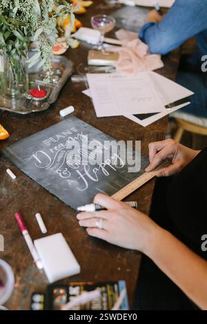 Hands working on a chalkboard with elegant lettering surrounded by art supplies and a fresh, inspiring atmosphere. Stock Photo