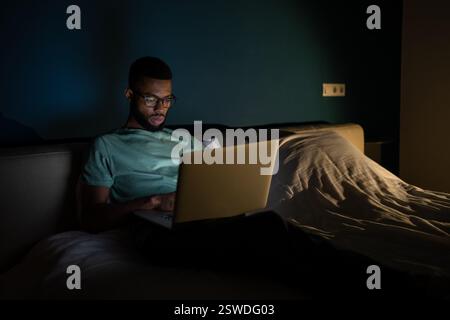 Black guy freelance IT developer using laptop at night, coding until late hours to meet deadline Stock Photo