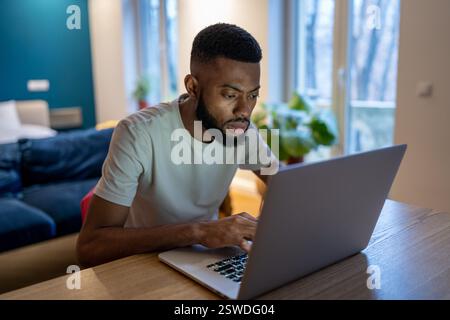 Focused African American guy freelancer working on laptop at home office, feeling overwhelmed Stock Photo