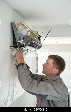 Installing air conditioner in apartment. Technician man in work uniform screwing air cooler to wall. Stock Photo