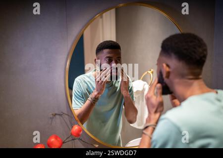 Unhappy worried young African man looking in mirror touching wrinkles on face Stock Photo