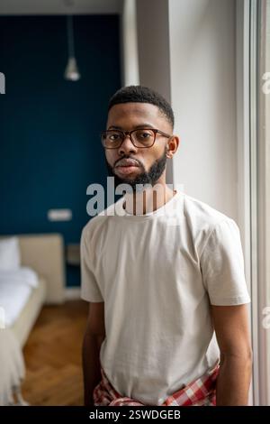 Portrait serious african american bearded man in eyeglasses in white t-shirt near window at home Stock Photo