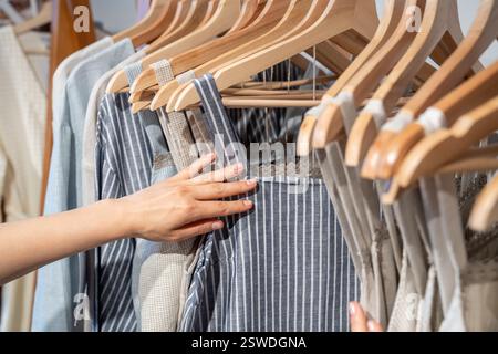 Organic cotton clothing hanging on rack, woman buying clothes made from recycled materials Stock Photo