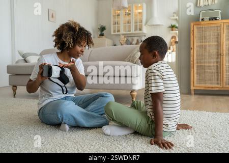Modern African American family mother and son sitting on floor with virtual reality headset Stock Photo