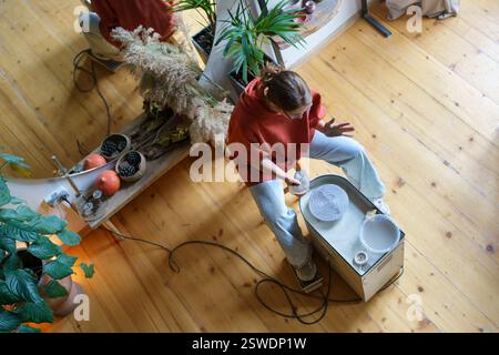 Young woman using electric pottery wheel machine while making ceramics at home Stock Photo