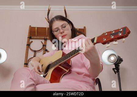 Young woman plays guitar performs in strumming style that is characteristic of acoustic classical guitar. Performance in home studio of musician. Low Stock Photo
