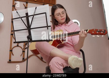 Young woman strums way to success as classical guitarist. She plays six string acoustic guitar with strumming style. Female guitar player is honing cr Stock Photo