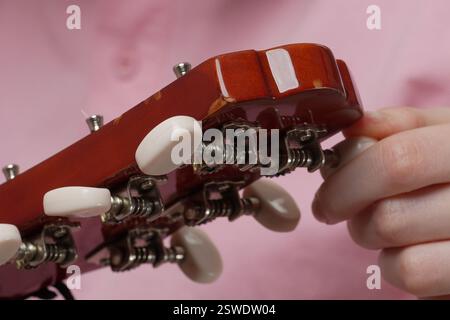 Extreme close-up female fingers tuning classical six string acoustic guitar, tightening and loosening strings before beginning to play guitar. Daily r Stock Photo