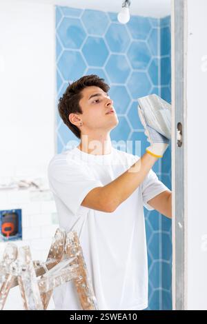Young guy laying tiles on walls in bathroom during renovation of house Stock Photo