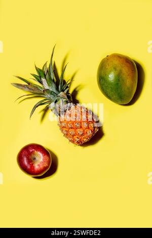 Mini pineapple, mango and apple on a solid yellow background Stock Photo