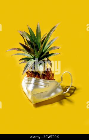 Mini pineapple in mask on a solid yellow background Stock Photo