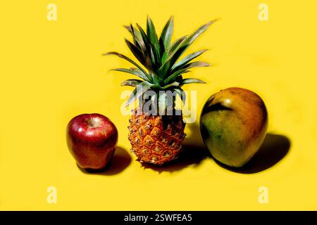 Mini pineapple, mango and apple on a solid yellow background Stock Photo