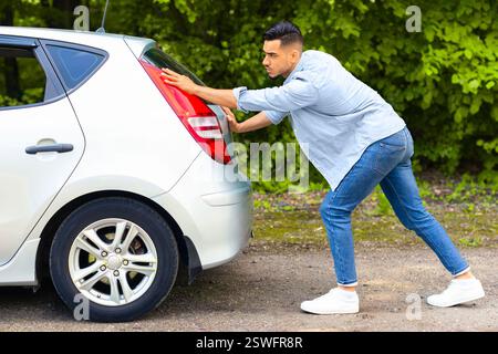 Arab guy pushing broken car, side view Stock Photo