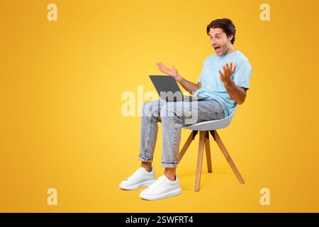 Excited guy using laptop celebrating success sitting on chair Stock Photo