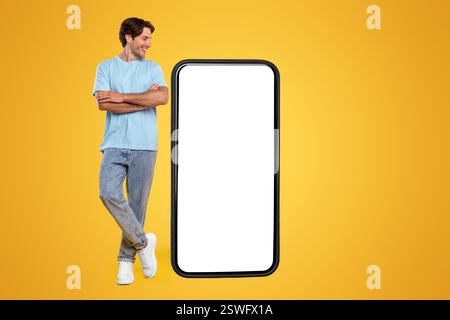 Guy standing near big empty smartphone screen with crossed hands Stock Photo