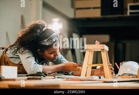 African American carpenter woman works on a wooden project using a laptop. utilize modern technology Stock Photo