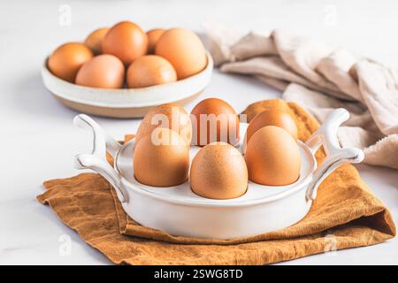 Raw brown eggs in a porcelain egg box on white background Stock Photo