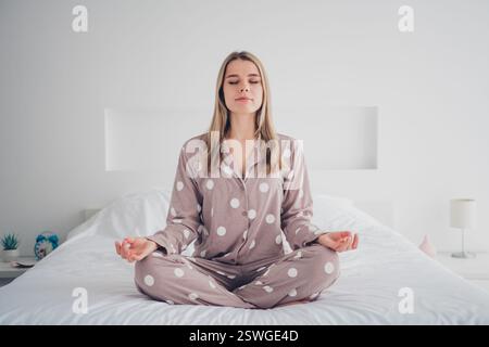 Young woman meditating in pajamas on cozy bed during serene morning at home Stock Photo