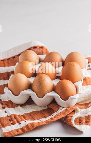 Raw brown eggs in a porcelain egg box on white background, vertical with copy space. Stock Photo