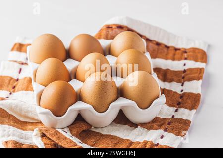 Raw brown eggs in a porcelain egg box on a striped cloth Stock Photo