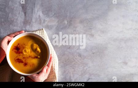Woman holding bowl of pumpkin soup with paprika spices and cream on white table. Kitchen napkin. Flat lay with copy space. Cream soup. Concept of tast Stock Photo