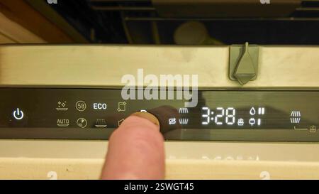 A male finger on the control panel of the dish washer. Switching programs on the dishwasher. Illuminated digital display buttons on the dishwasher Stock Photo