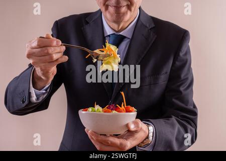 Professional senior man eating a fresh salad, promoting healthy eating habits in a corporate lifestyle. Stock Photo