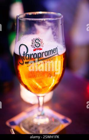 A glass of Staropramen beer on a coaster in a dimly lit bar with colorful ambient lighting and blurred pub  background Stock Photo