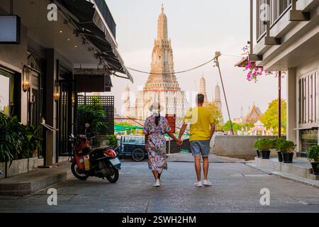 Couple walks hand in hand through charming streets towards the iconic Wat Arun in Bangkok Stock Photo