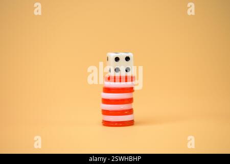 A stack of poker chips topped with dice against an orange backdrop, symbolizing chance, games, and entertainment, tiddlywinks Stock Photo
