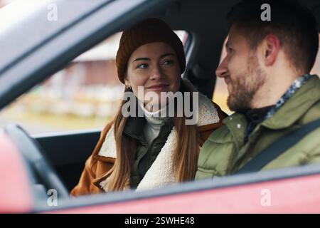 Smiling couple dressed warmly sitting inside car with a scenic background and enjoying cozy winter day, man and woman wearing winter clothing and engaging in a light conversation Stock Photo