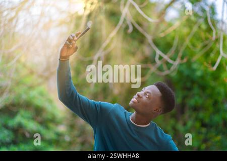 Young attractive black man wearing green t-shirt in a park taking a selfie smiling, happiness concept. Stock Photo