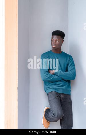 A man is leaning against a wall with his arms crossed in a confident posture. Stock Photo