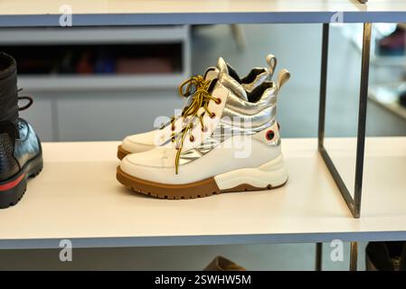 White winter boots with metallic details and yellow laces stylishly displayed on shop shelf in a retail setting, footwear fashion concept Stock Photo