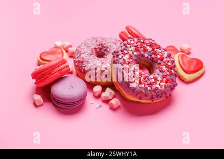 An eye-catching arrangement of colorful macarons and donuts on a pastel pink background. Perfect for showcasing desserts or sweet treats with a playfu Stock Photo