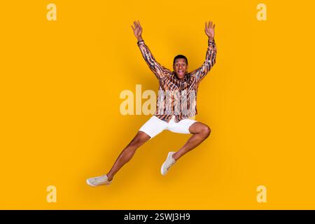 Dynamic young man jumping with expressive joy against yellow background showing exciting casual summer fashion Stock Photo