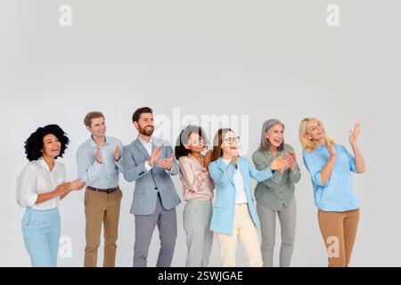 Diverse group of professionals in a friendly atmosphere, smiling and clapping together on a grey background Stock Photo