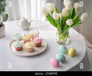 A delightful table setting featuring pastel cupcakes and colored eggs amidst blooming tulips. Stock Photo