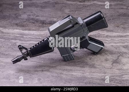 A dark metallic toy gun placed on a wooden surface against a black background, featuring detailed craftsmanship and studio lighting for enhanced empha Stock Photo
