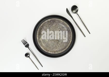 Top view of brown marble plate, black plate and cutlery on white background. Food presentation, stone tray. Table setting, copy space, flat lay. Stock Photo
