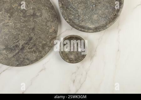 Top view of brown marble tray, plate and bowl on white marble background. Food presentation, dishes, stone tray. Copy space, flat lay. Stock Photo