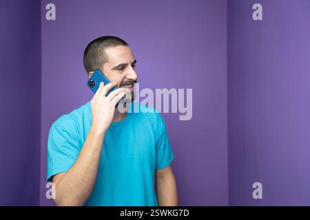 A young man engaged in a phone conversation within a vibrant and colorful purple room, Stock Photo