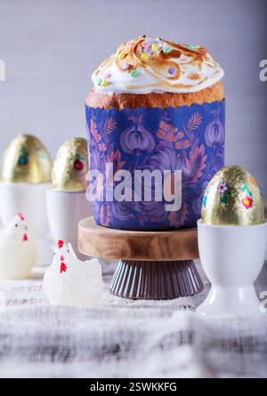 Easter cake, chocolate eggs in gold foil and chicken-shaped candles on a light background. Traditional Easter cake with meringue and colored sugar dec Stock Photo