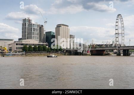 London's Thames River, showing the London Eye, Royal Festival Hall, and a construction site.  A small boat is on the water. Stock Photo