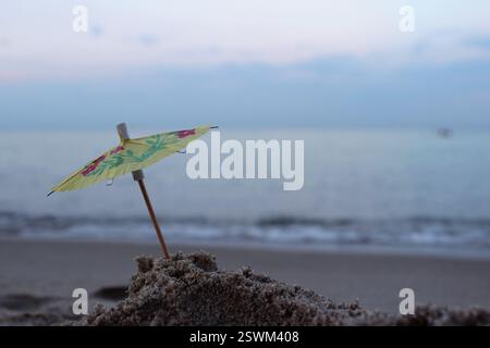 An umbrella from a cocktail in the sand on the beach against the background of sea waves. Concept, summer, rest Stock Photo