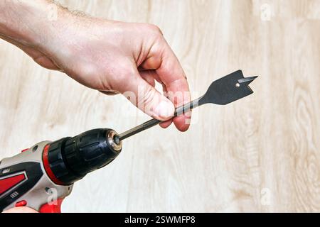 Cordless drill with spade bit held by hand. Stock Photo