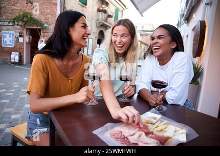 Three female friends enjoying wine and charcuterie in italian town Stock Photo